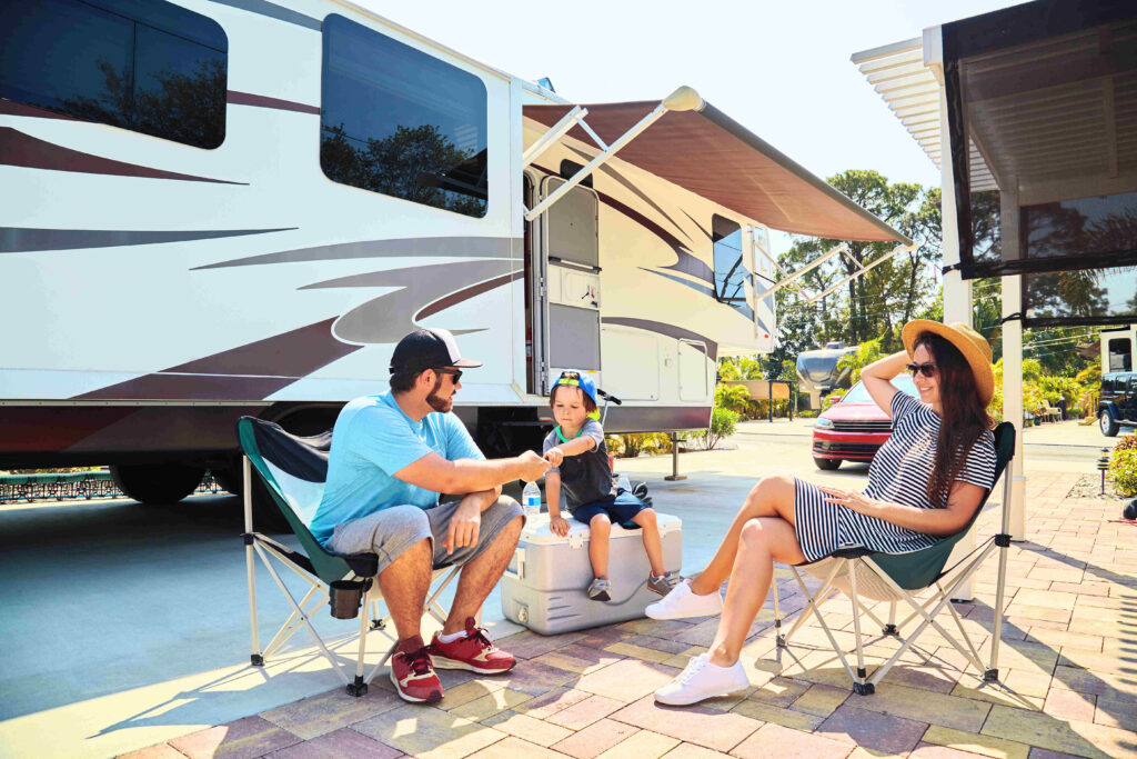 Family relaxing outside their travel trailer at an RV park, enjoying a sunny day together—travel trailer insurance lifestyle image